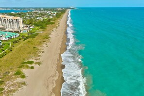 A coastal hotel with a beachfront view, a long sandy beach, and a clear blue ocean.