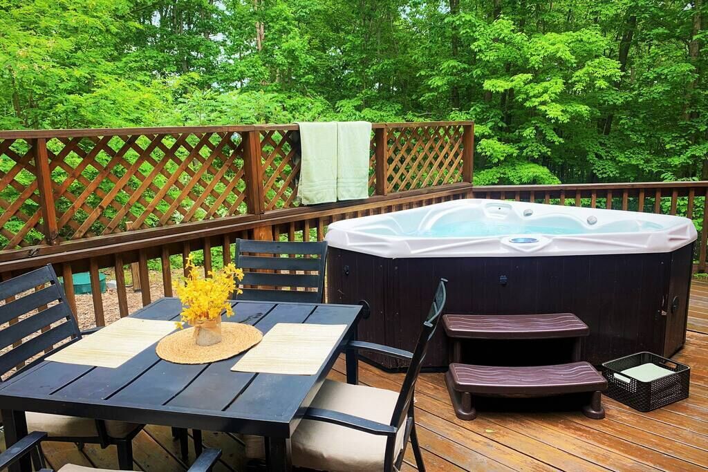 Une terrasse en bois avec un jacuzzi, une table et des chaises, et un banc.