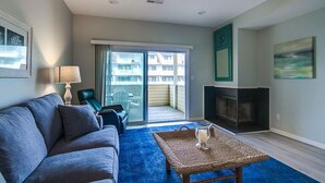 A living room with a sofa, a coffee table, a fireplace, and a sliding glass door leading to a balcony. - Ocean View and only steps to the sand !! (Fenwick Island)