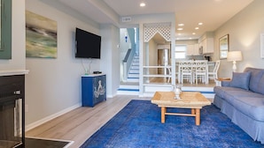 A modern living room with a blue rug, a flat-screen TV, a fireplace, and a staircase leading to a dining area. - Ocean View and only steps to the sand !! (Fenwick Island)