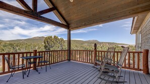 Eine Holzterrasse mit Tisch und Stühlen mit Blick auf eine gebirgige Landschaft.
