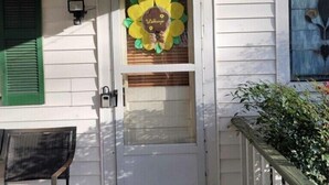 A white door with a flower decoration and a "Welcome" sign, a bench, and a wooden deck. - Steve & Katie Riley Guest House, Breaux Bridge, 2 Bd, 1.5 Ba. Welcome!  Sleeps 6 (Breaux Bridge)