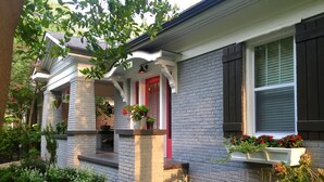 Une maison avec une façade en briques, une porte rouge et un porche agrémenté de plantes en pot.