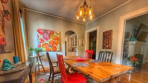 Un coin repas avec une table en bois, des chaises rouges, un lustre et un tableau coloré accroché au mur.