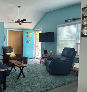 A living room with a ceiling fan, a television, a blue door, and a window with blinds.