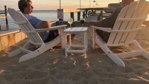 Two white Adirondack chairs facing a pier with a 'CAUTION' sign and a 'NO DIVING' sign. A table with a glass of red wine is between them. - Middle of Dewey ,On the Bay, Close to the Beach  (Dewey Beach)