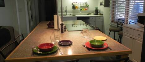 A kitchen with a central island, a dining area with chairs, and a window with blinds.