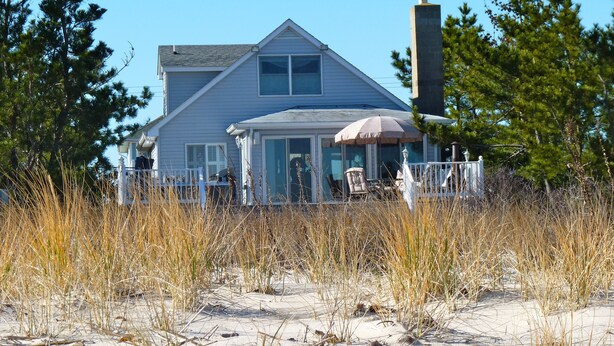 A coastal house with a covered patio, surrounded by tall grasses and trees.
