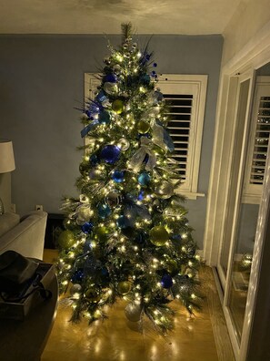 A Christmas tree with lights and ornaments in a room with a window and a lamp.
