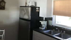 A compact kitchen with a refrigerator, coffee maker, and a window with blinds. - ON the Beach, 2nd Floor, Elevator, Heated swimming pool and Spa, Freshly painted (Longboat Key)
