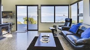 A modern living room with a large window, a fireplace, a sofa, and a coffee table. - Park Beach Retreat - Ideal for couples (Dodges Ferry)