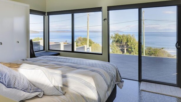 A bedroom with a bed, large windows, and a view of the sea. - Park Beach Retreat - Ideal for couples (Dodges Ferry)