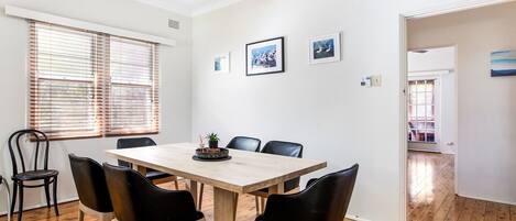 A dining area with a wooden table and black chairs, white walls, and a wooden floor.