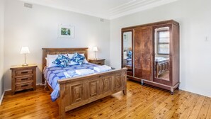 Un dormitorio con una cama de madera, dos mesitas de noche con lámparas, un armario de madera y un espejo.