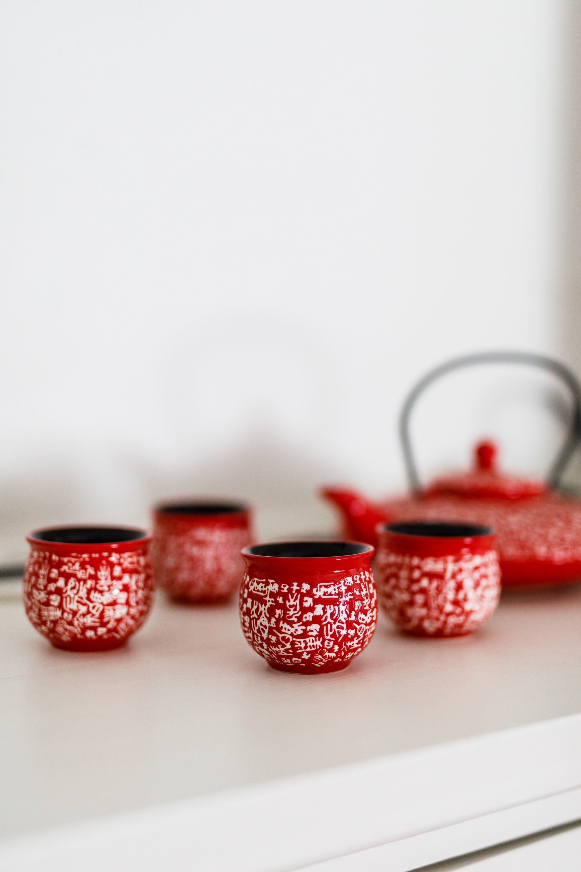 A white shelf with four red cups and a red teapot.