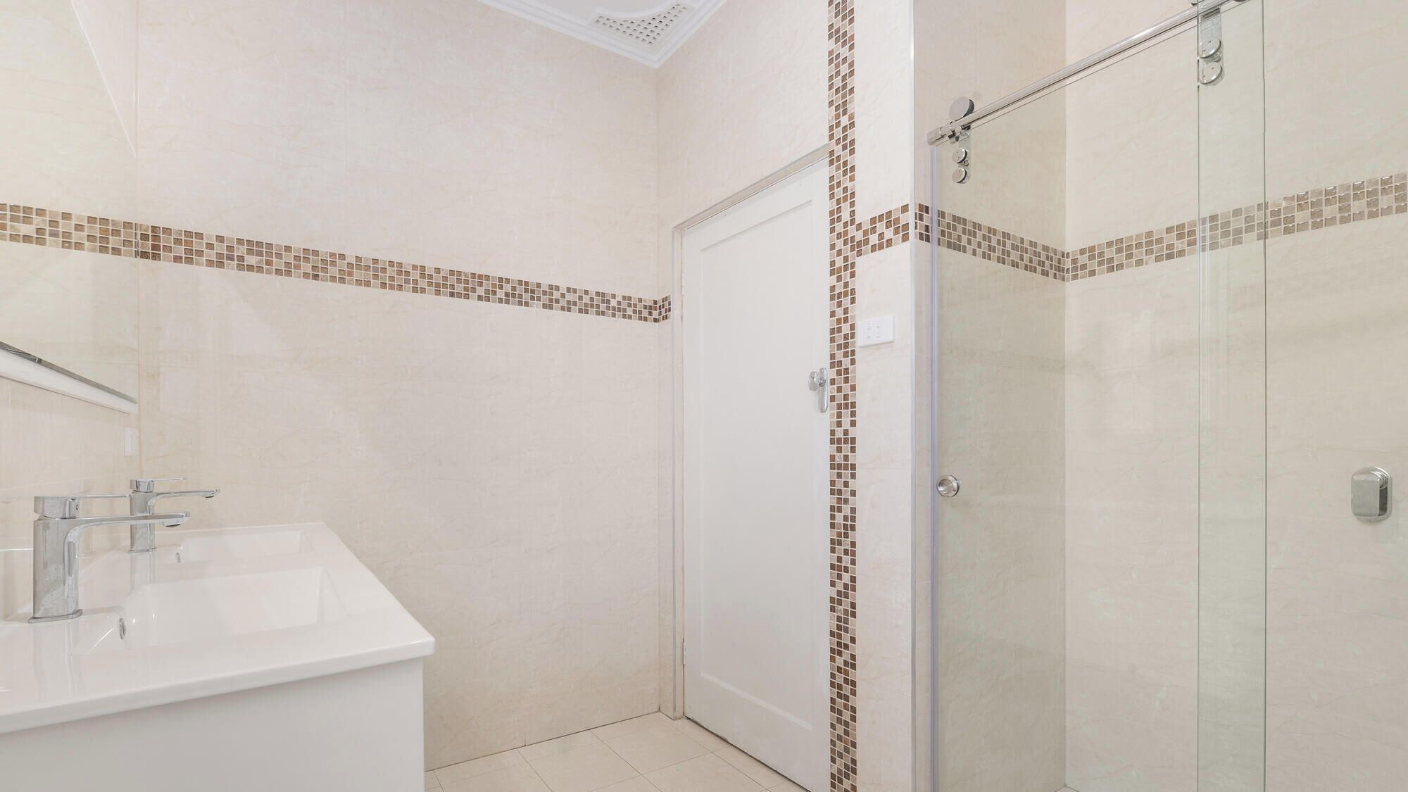 A bathroom with a white sink, a mirror, and a shower with a glass door.