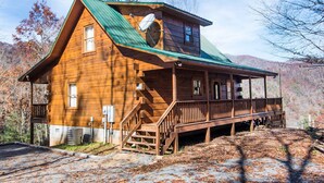 Une cabane en bois avec un toit vert, une véranda et un escalier menant à l’entrée.