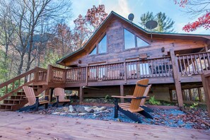 Una cabaña de madera con balcón, dos sillas Adirondack y una chimenea de piedra.