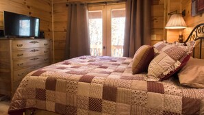 Une chambre à coucher dans une cabane en bois, avec une couvre-lit matelassé, une commode, un téléviseur et une fenêtre avec des rideaux.