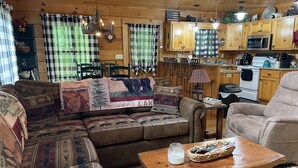L’intérieur chaleureux d’un chalet comprend un grand canapé, une table à manger et un coin cuisine doté de meubles et d’appareils électroménagers en bois.