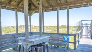 Eine Holzterrasse mit Picknicktisch und Bänken, mit Blick auf einen Strand mit Dünen.