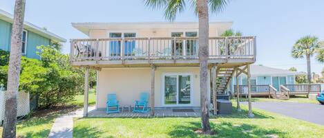 A two-story building with a balcony, outdoor seating, and palm trees.