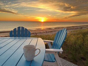 Una mesa con una taza y dos sillas mirando al atardecer sobre el océano.