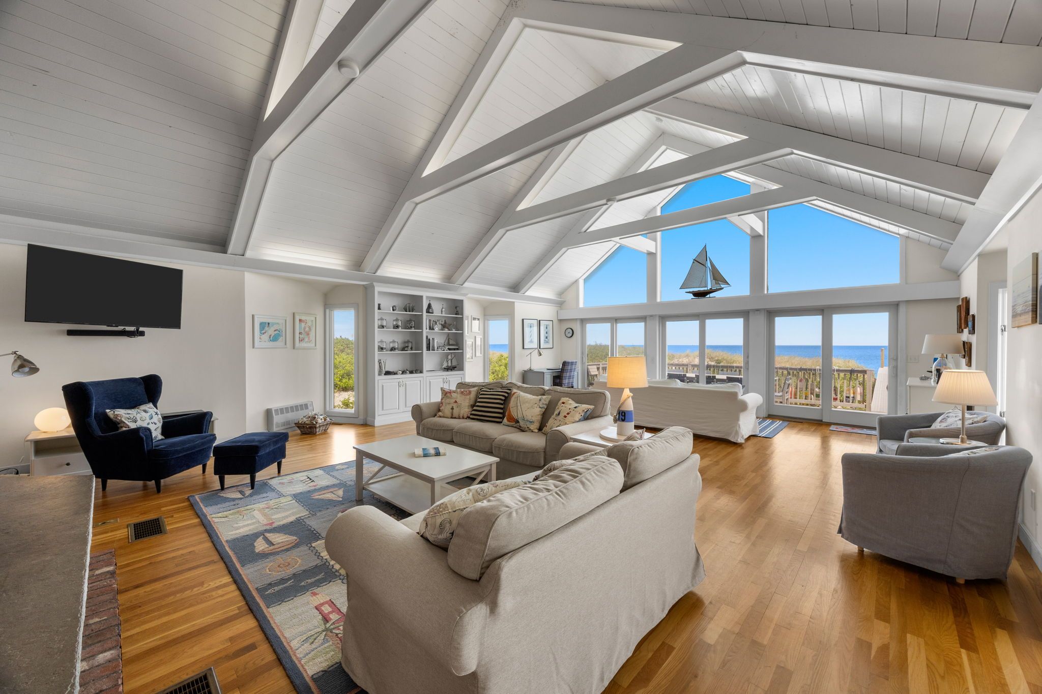 Un salon spacieux avec un haut plafond, un plancher en bois et une grande fenêtre donnant sur la mer.