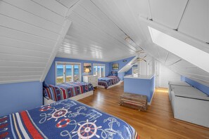 Un dormitorio con techo inclinado, suelo de madera y vistas al mar a través de amplios ventanales.