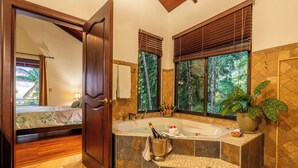 Une salle de bain avec une grande baignoire, une plante en pot et une fenêtre avec des stores.