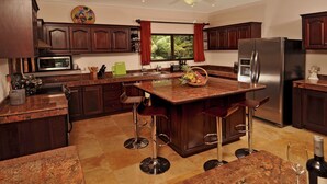 Une cuisine moderne avec des meubles en bois foncé, un réfrigérateur en acier inoxydable, un plan de travail en granit et un îlot central doté de tabourets de bar.