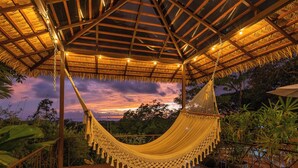 Un hamac sous une pergola en bois, avec vue sur le coucher du soleil.