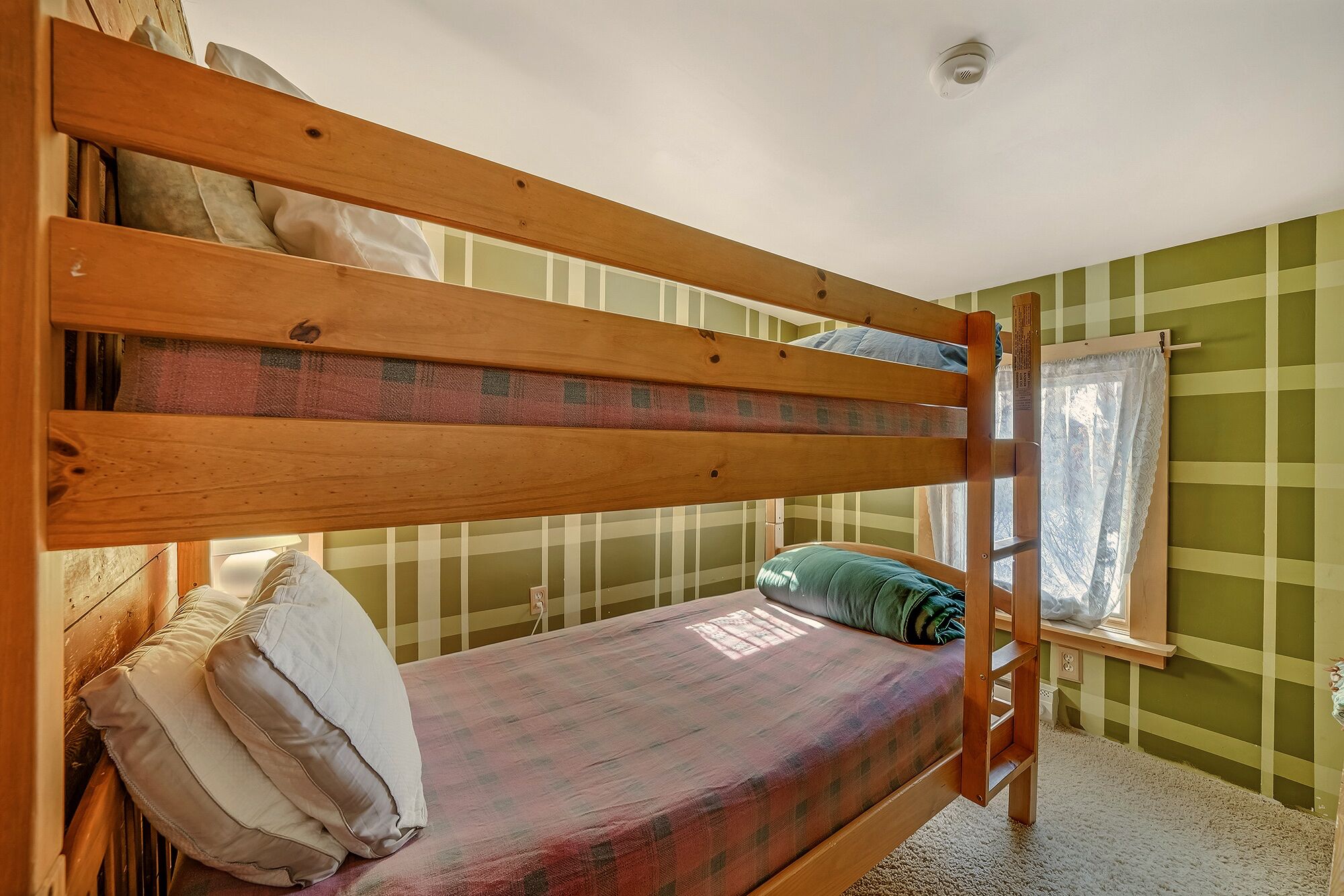 Un lit superposé avec un matelas et des oreillers, une fenêtre avec un rideau et un mur à rayures vertes.
