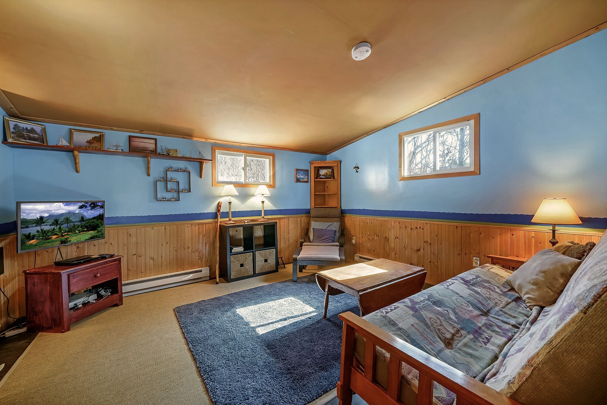 A cozy room with a television, wooden furniture, a blue carpet, and a window with a view.