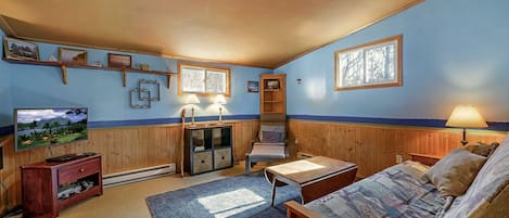 A cozy room with a television, wooden furniture, a blue carpet, and a window with a view.