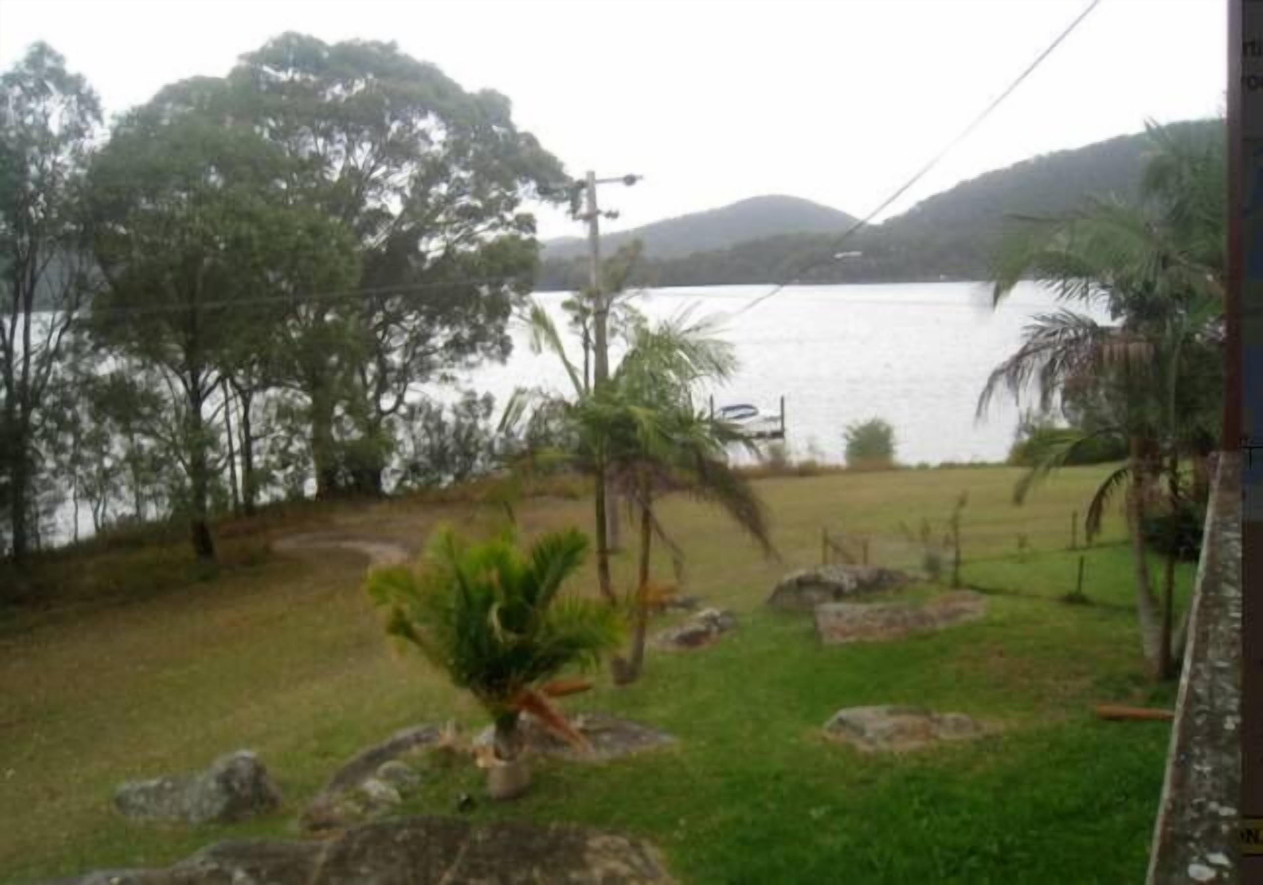 A view of a lake with trees and rocks in the foreground, and hills in the background.