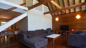 A spacious living area with a wooden ceiling, a sofa, a coffee table, and a TV.