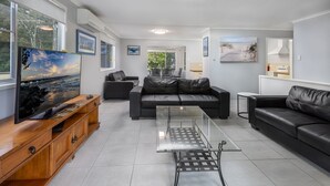 A modern living room with a glass coffee table, leather sofas, and a wooden entertainment unit. - Beach Hound (pets welcome) (Toogoom)