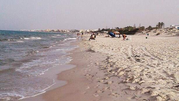Una playa arenosa con huellas y algunas personas a lo lejos.