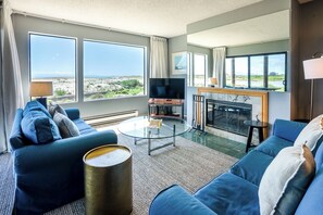 A living room with a sofa, a coffee table, a TV, a fireplace, and large windows with a view.