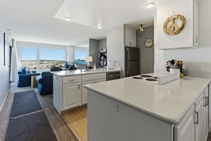 A modern kitchen with white cabinetry, a large island, and a view of the beach.