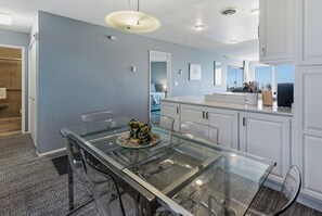 A modern kitchen with white cabinets, a glass dining table, and a view of the city.