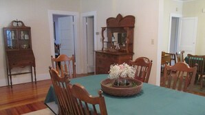 Comedor con una mesa dispuesta para seis personas, rodeada de sillas de madera. Un aparador grande con puertas de vidrio se encuentra a la izquierda, y un espejo cuelga en la pared sobre la mesa.