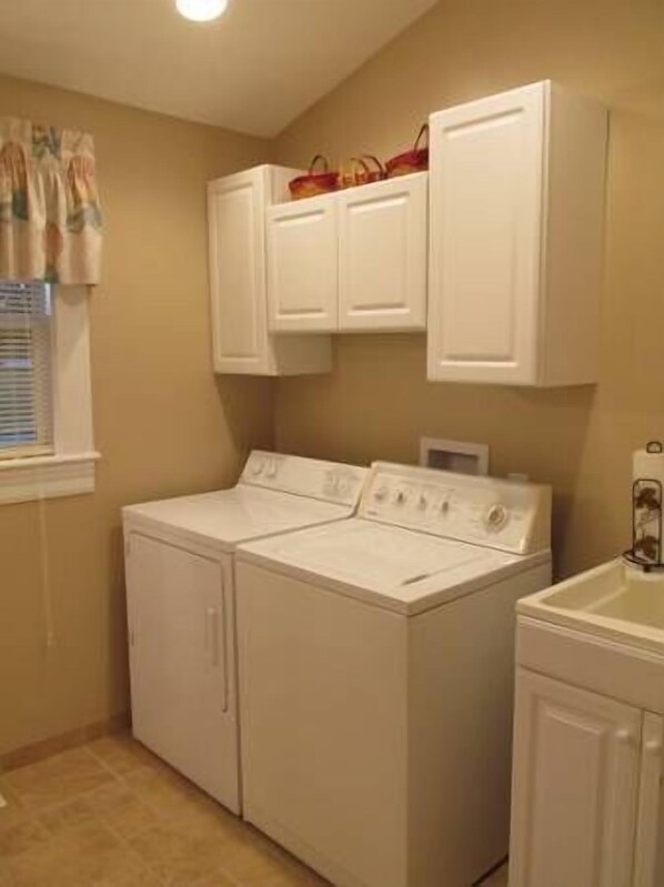 Une buanderie équipée de deux machines à laver, d’un sèche-linge et de placards blancs situés en hauteur.