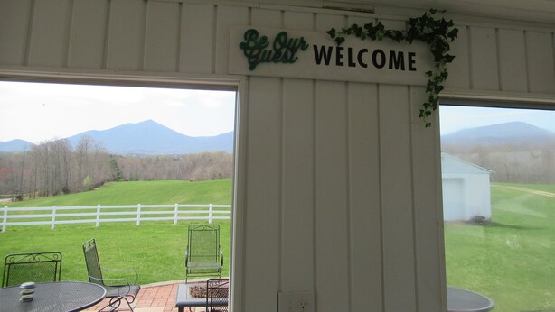 Un área de patio techada con un letrero que dice "Welcome", mobiliario exterior y vistas a una cadena montañosa.