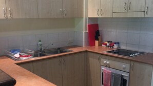 A kitchen with light wooden cabinets, a stainless steel sink, a countertop with a dish rack, and an oven with towels hanging. - Golf Course Apartment/Within Trinity Links Resort/ Selfcontained (White Rock)