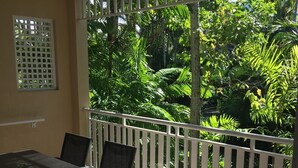 A balcony with a glass table and chairs, surrounded by a white railing, overlooking a lush garden. - Golf Course Apartment/Within Trinity Links Resort/ Selfcontained (White Rock)
