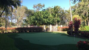 A well-maintained golf course with a clear putting green, surrounded by lush greenery and a white fence. - Golf Course Apartment/Within Trinity Links Resort/ Selfcontained (White Rock)