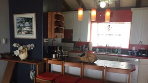 Een keuken met een houten kookeiland, rode fauteuils met kussens, een koffiezetapparaat en een raam met uitzicht.
