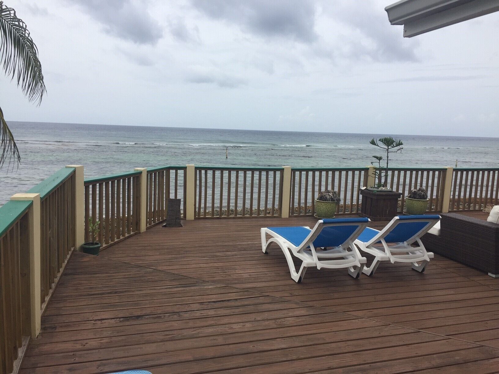 A wooden deck with a railing, two lounge chairs, and a view of the ocean.